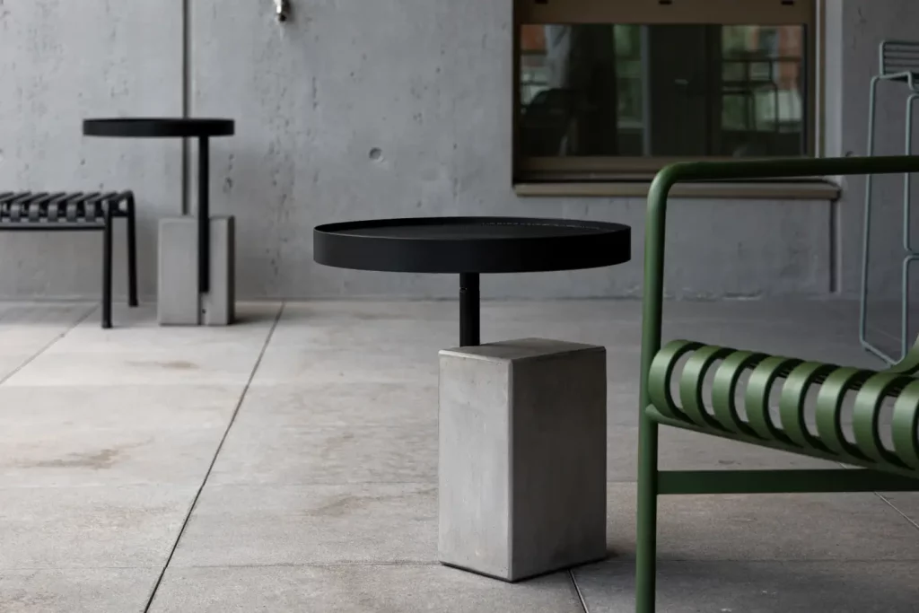 Le bout de canapé Twist en béton et métal noir à coté d'une chaise en métal verte sur un balcon, table d'appoint en béton
