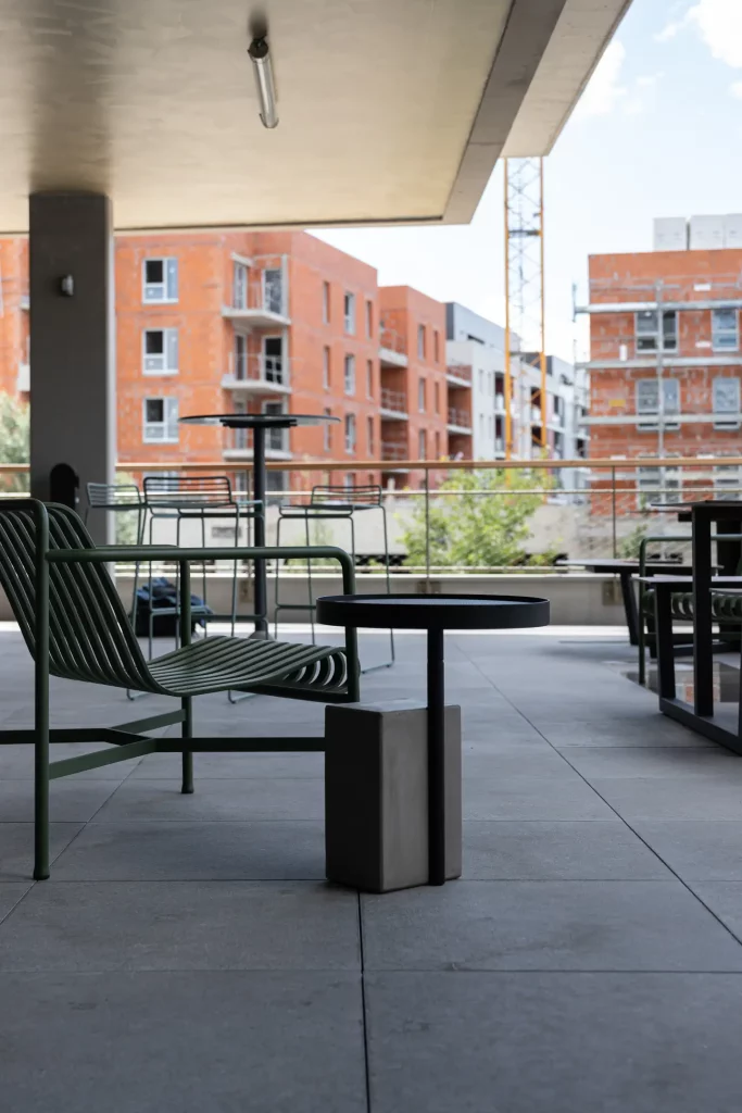 Une terrasse couverte meublé de tables et chaises en métal qui accompagne le guéridon en béton Twist