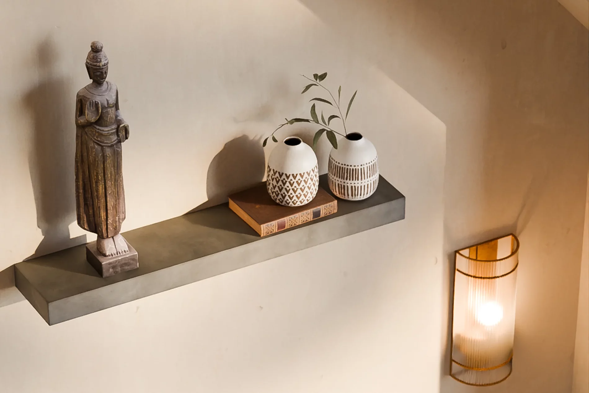 Étagère Sliced en béton avec une statuette en bois, un livre et deux vases en céramique.