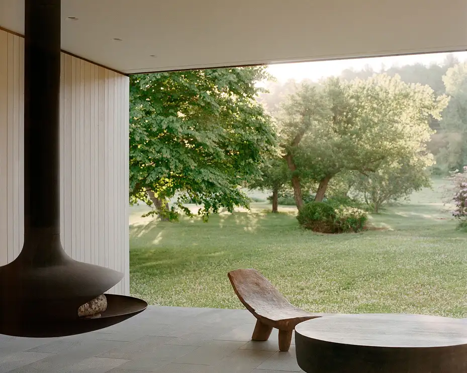 Intérieur minimaliste associant béton et bois avec cheminée suspendue et baie vitrée sur jardin