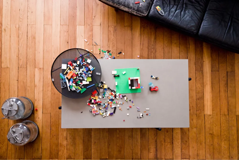 Le plateau en béton de la table basse Twist recouvert de brique Lego à coté d'un canapé en cuir vintage