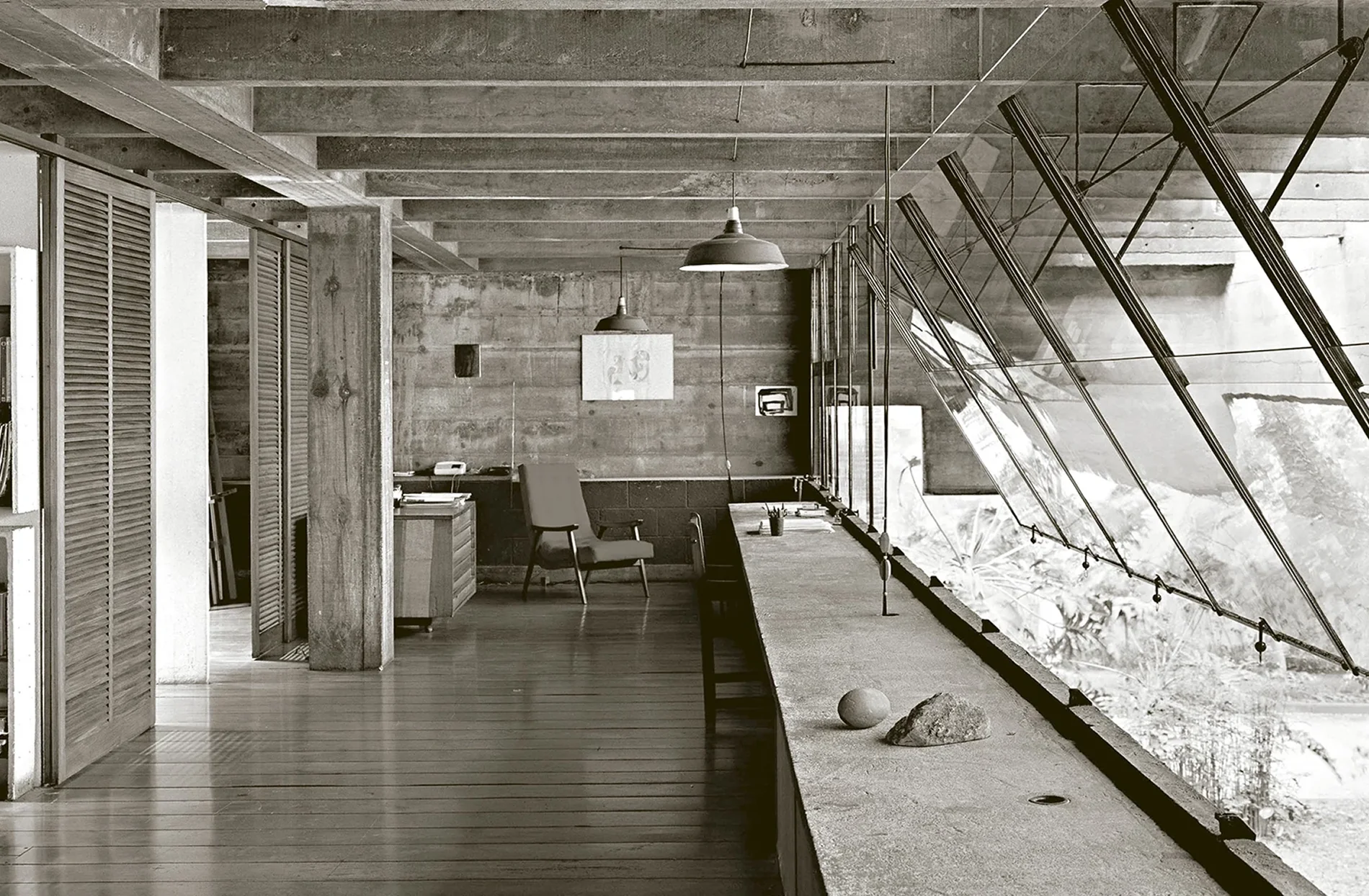 Bureau brutaliste avec un long plan de travail en béton brut, un plancher en bois et une verrière inclinée