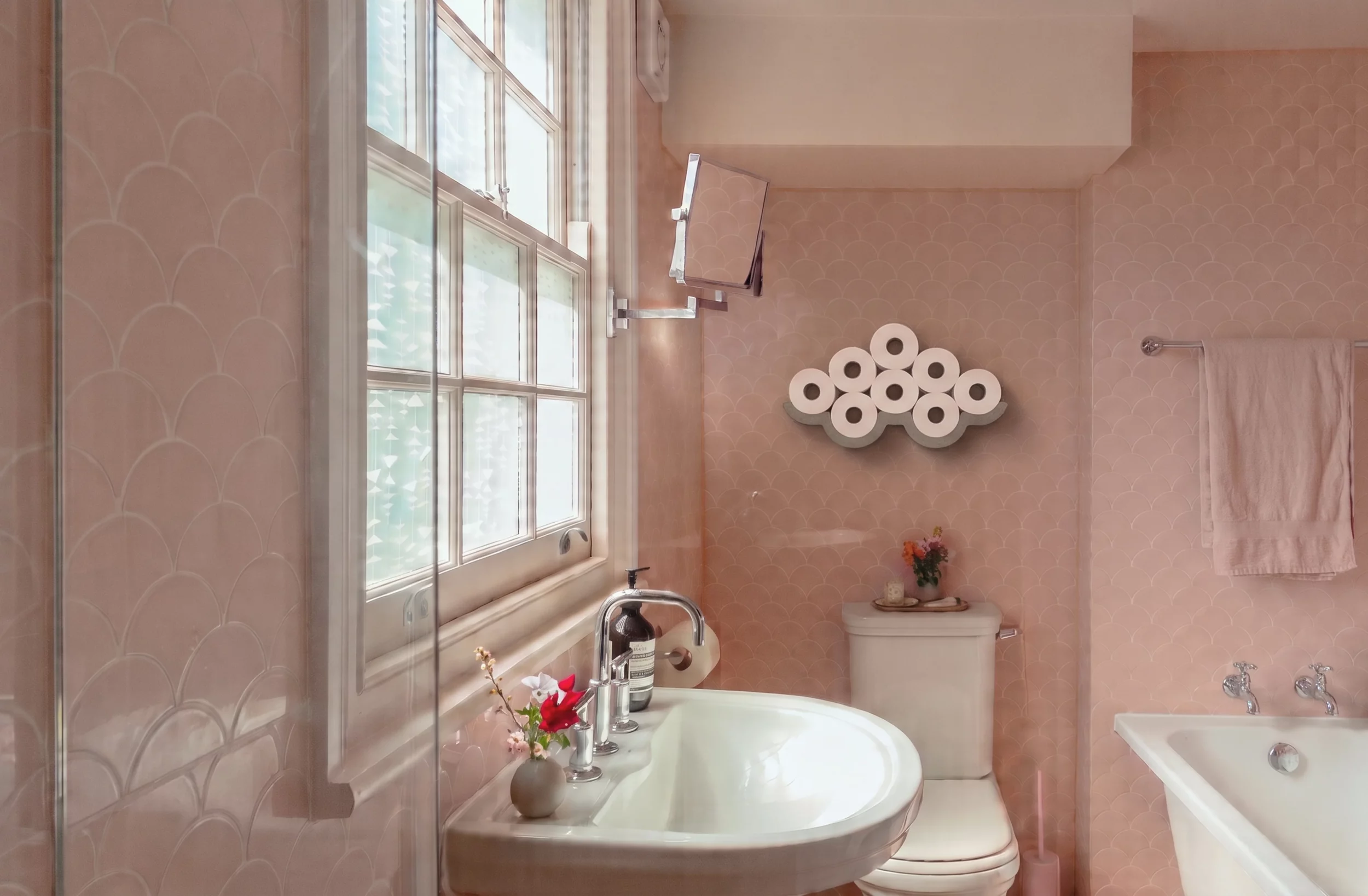 Porte-papier toilette Cloud en béton rempli de rouleaux, dans une salle de bain au carrelage rose.